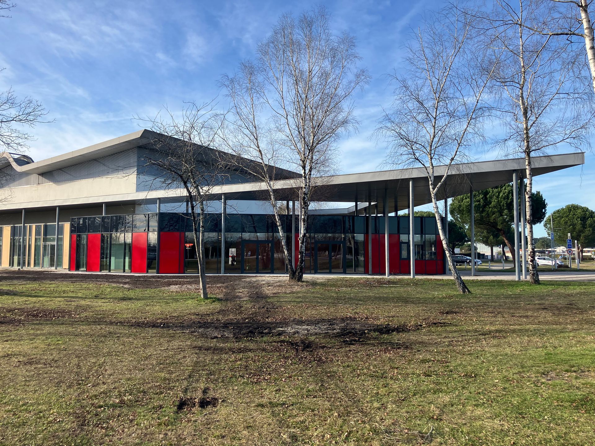 Bâtiment moderne aux murs de verre, aux touches de rouge et au toit plat, se détachant sur un ciel bleu.