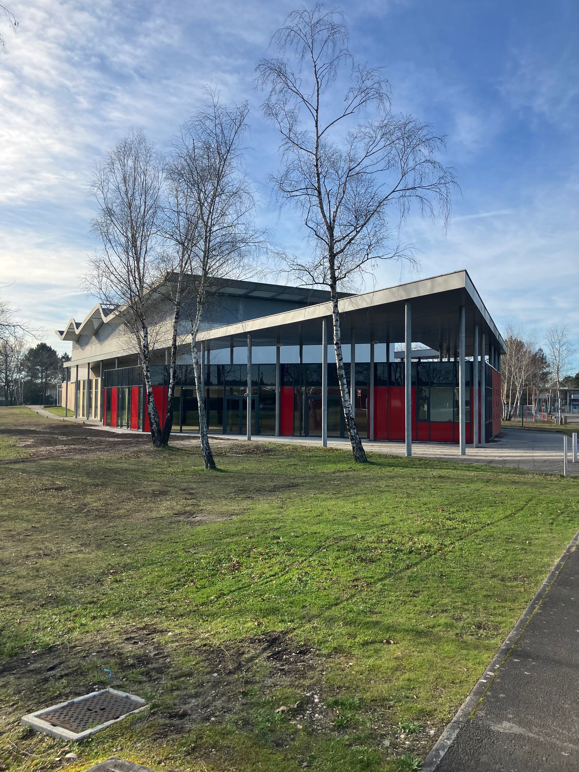 Bâtiment aux accents rouges et aux fenêtres en verre, avec des arbres devant, se détachant sur un ciel bleu.