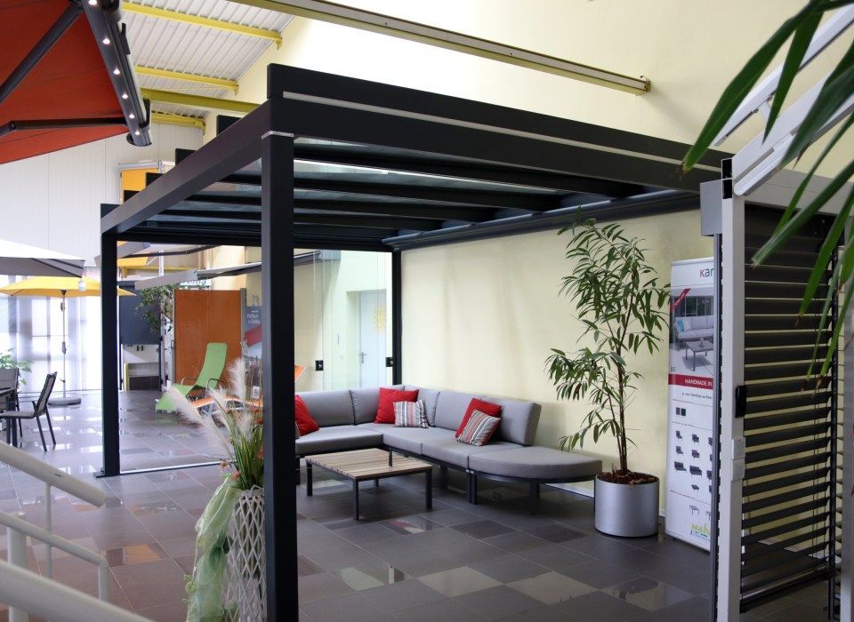 Schwarze Pergola über dem Sitzbereich im Freien, graues Ecksofa, Couchtisch, Topfpflanze, Inneneinrichtung.