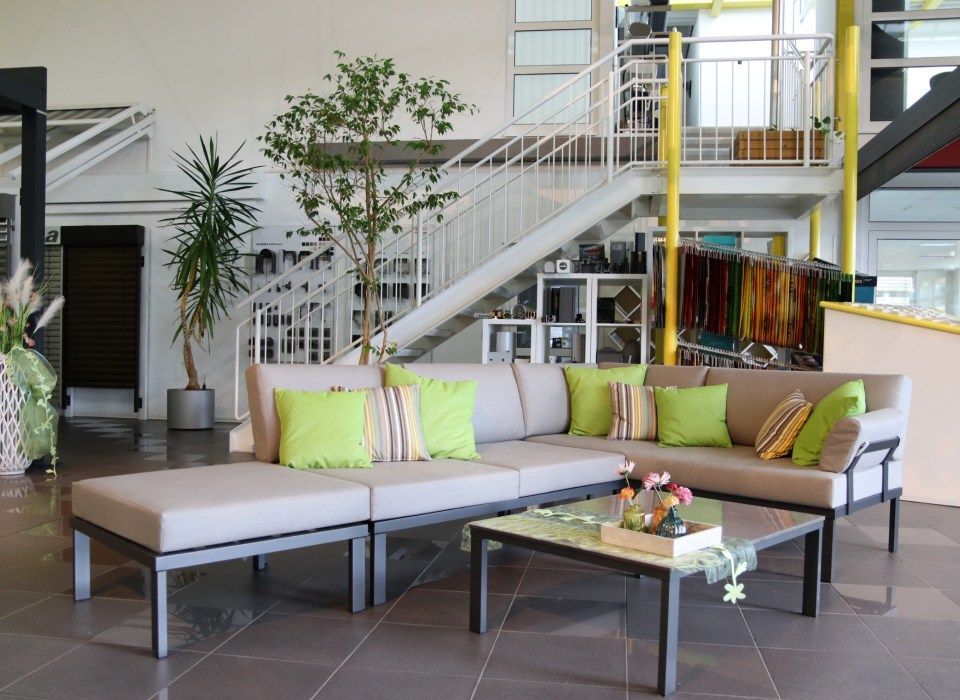 Lounge-Set mit grauen Kissen und limettengrünen Zierkissen, Couchtisch, in einem Ausstellungsraum mit Treppenhaus.