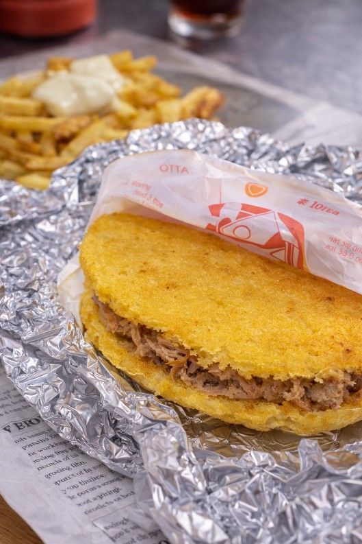 Una arepa de color amarillo dorado rellena de carne desmenuzada, envuelta en papel y papel de aluminio