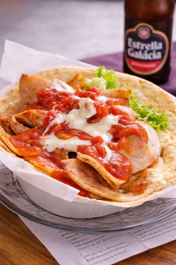 Un plato de pollo servido en un bol de pan plano, cubierto con salsa de tomate y queso fundido