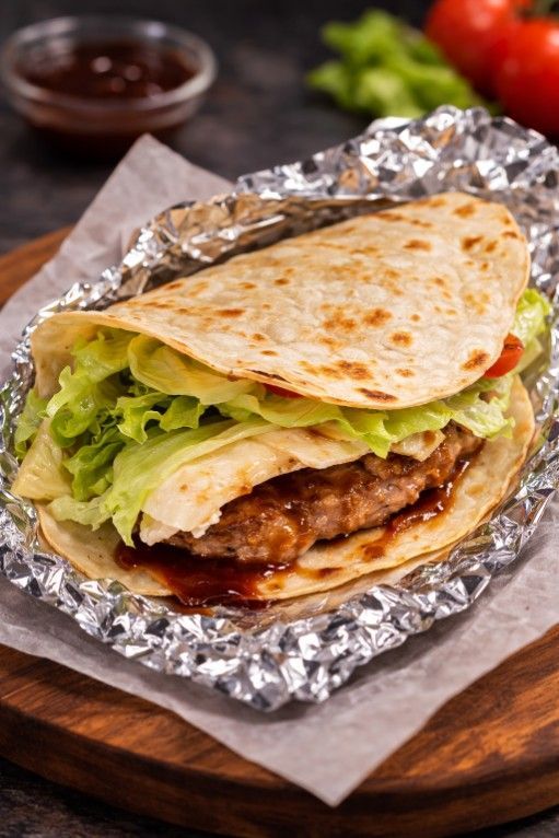Una tortilla de harina doblada, rellena de una hamburguesa de carne, lechuga y salsa barbacoa