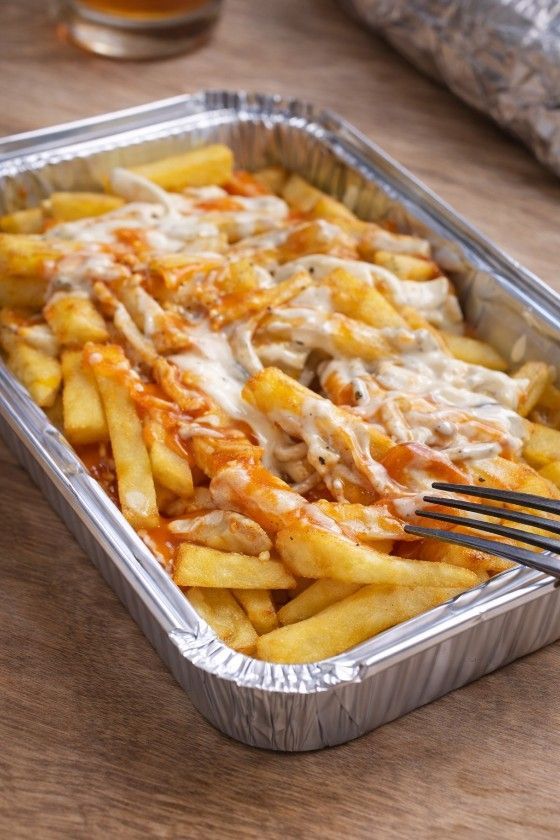 Un recipiente metálico para llevar con patatas fritas cubiertas de pollo, queso blanco fundido y salsa rojA