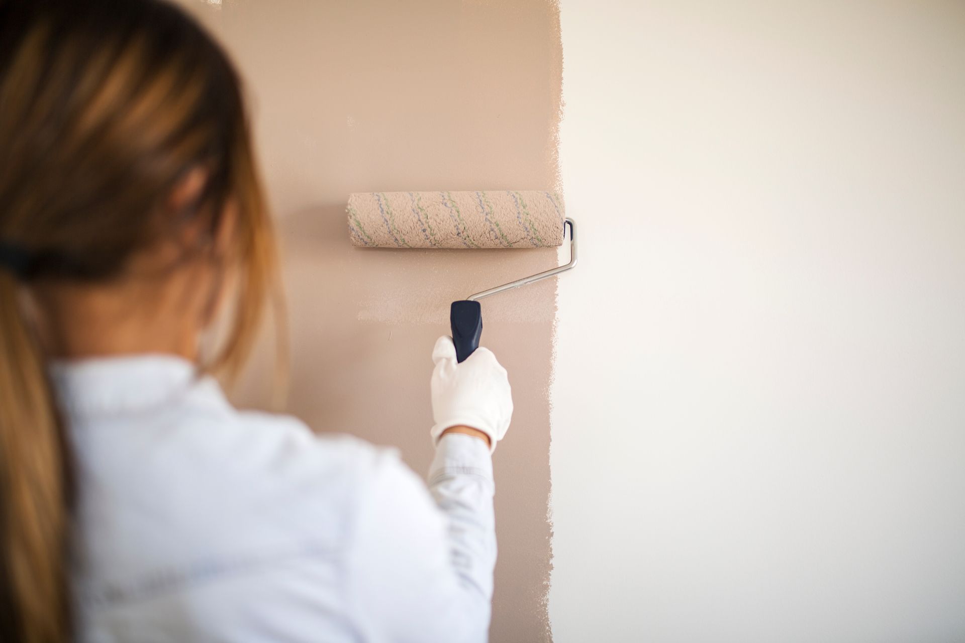 Maler auf Leiter streicht eine graue Wand; auf dem Boden stehen Farbeimer und Abdeckplanen.