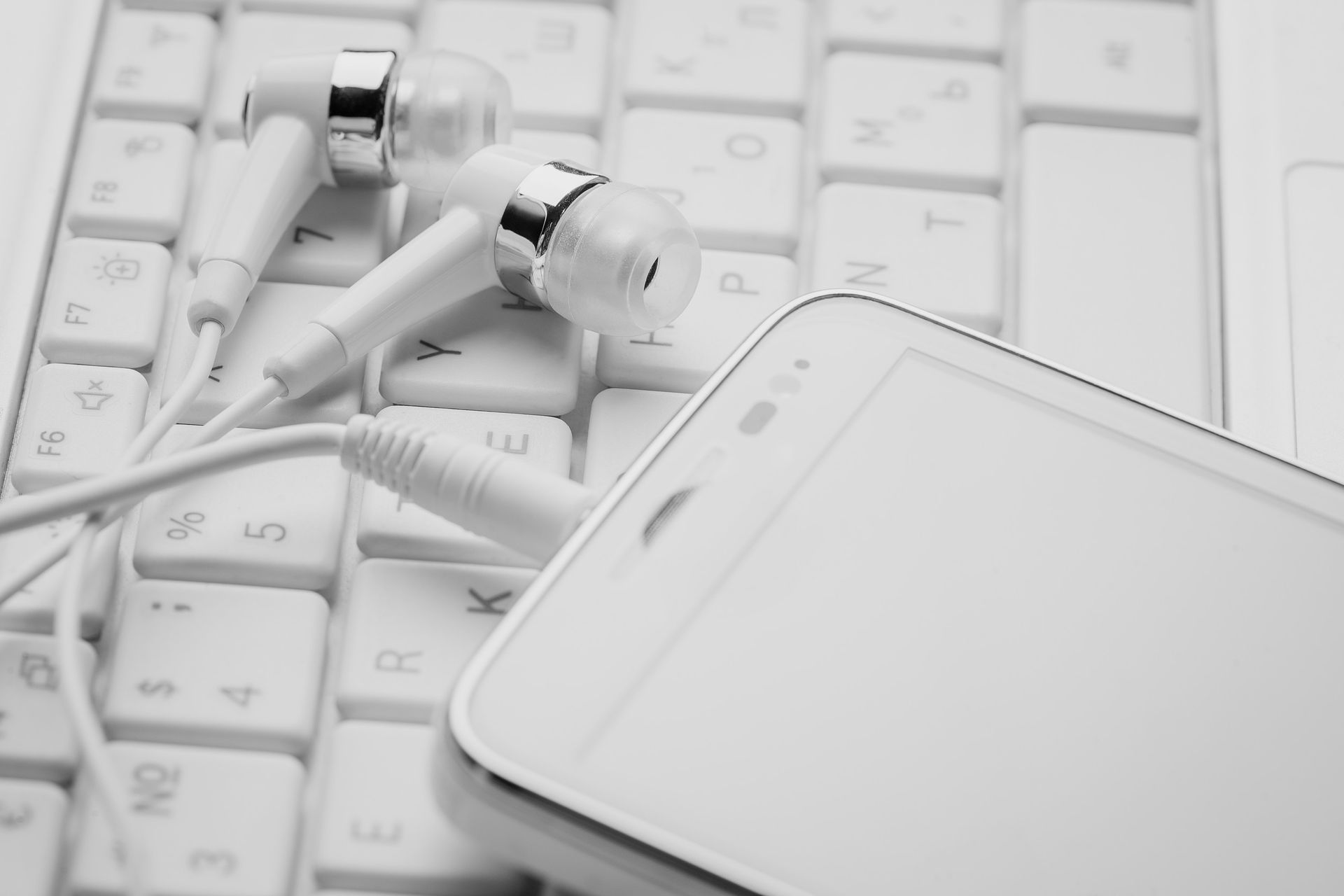 Un teléfono celular y auriculares están conectados a un teclado blanco.