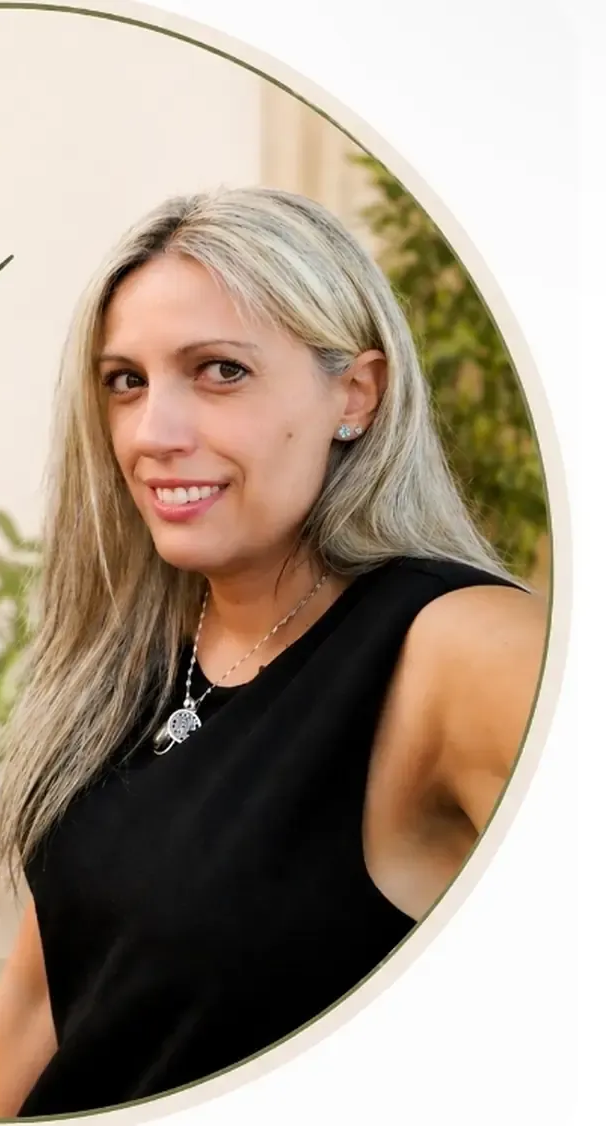 Retrato de una mujer sonriente con cabello plateado, vestida con una blusa negra sin mangas, sobre un fondo claro.