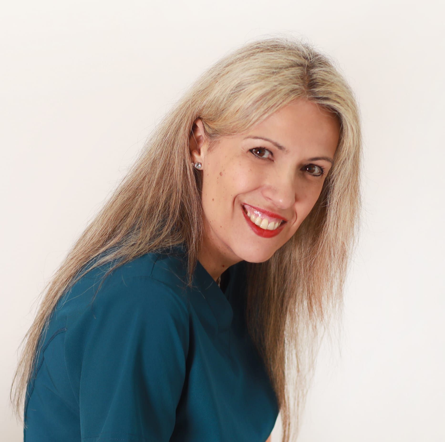 Mujer sonriente con una blusa color turquesa y cabello rubio largo sobre un fondo blanco.