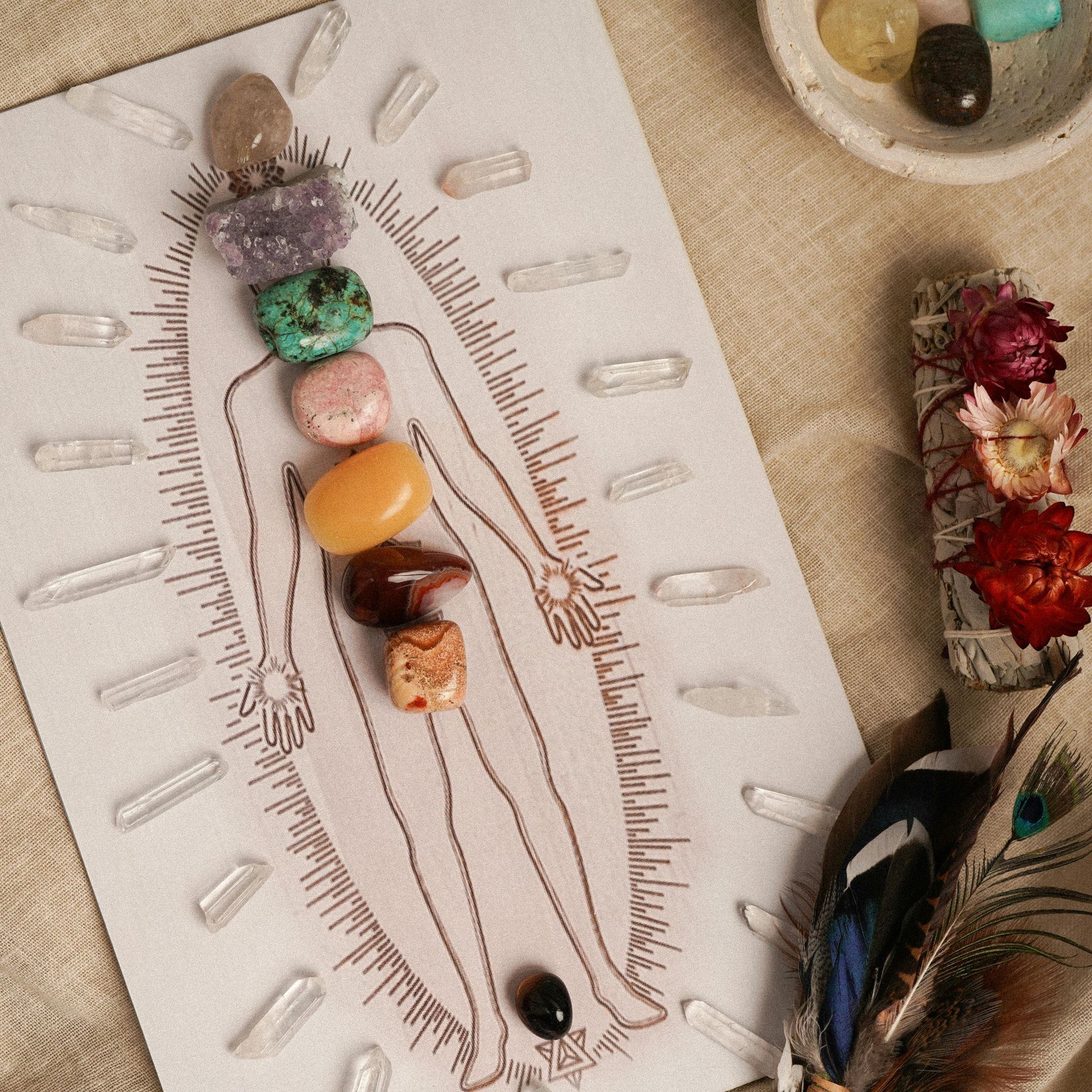 Gráfico de chakras con cristales y plumas sobre papel con flores secas y conchas sobre una superficie beige.