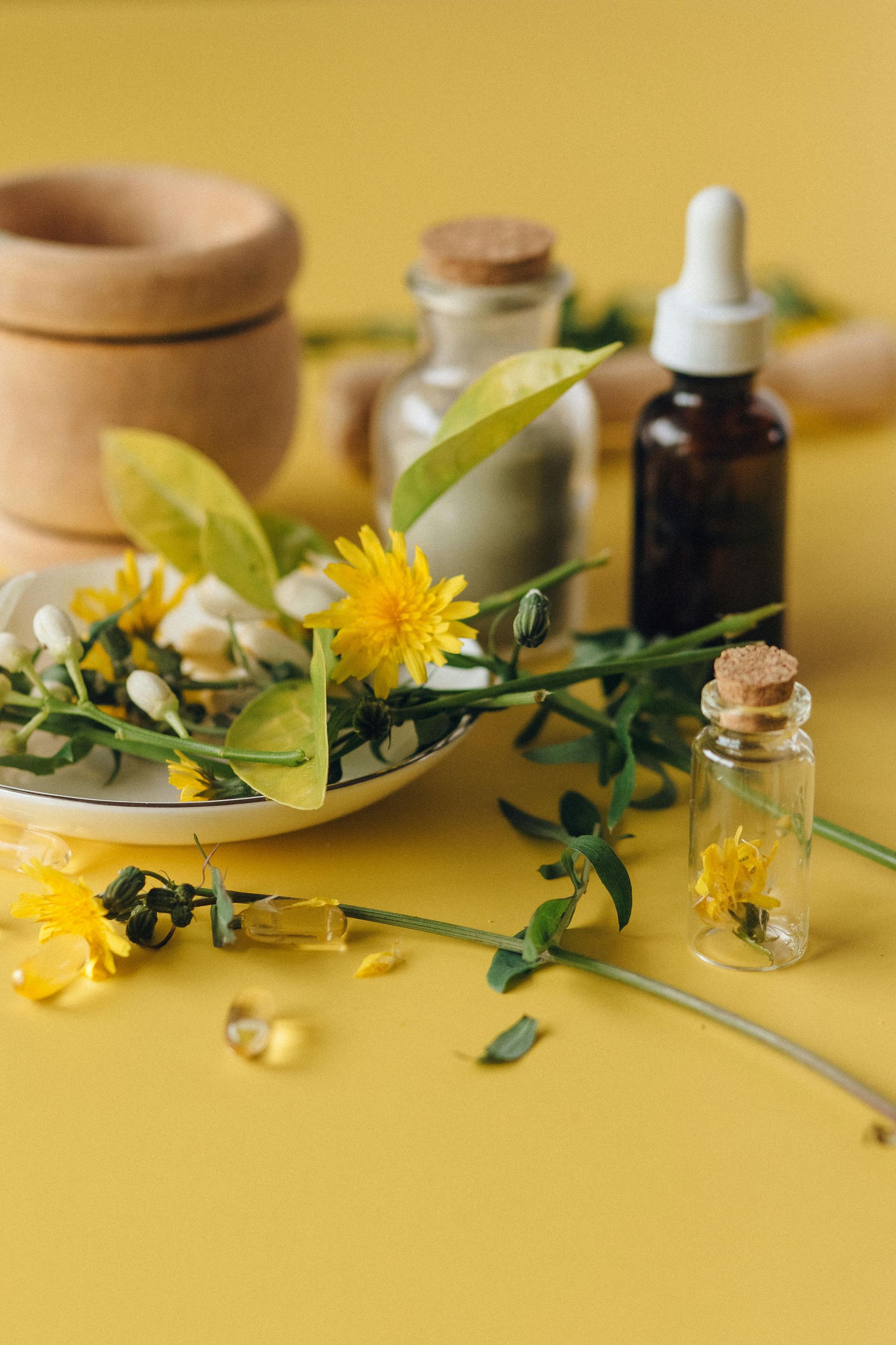Flores amarillas, ramitas verdes y pequeñas botellas de vidrio dispuestas sobre una superficie amarilla