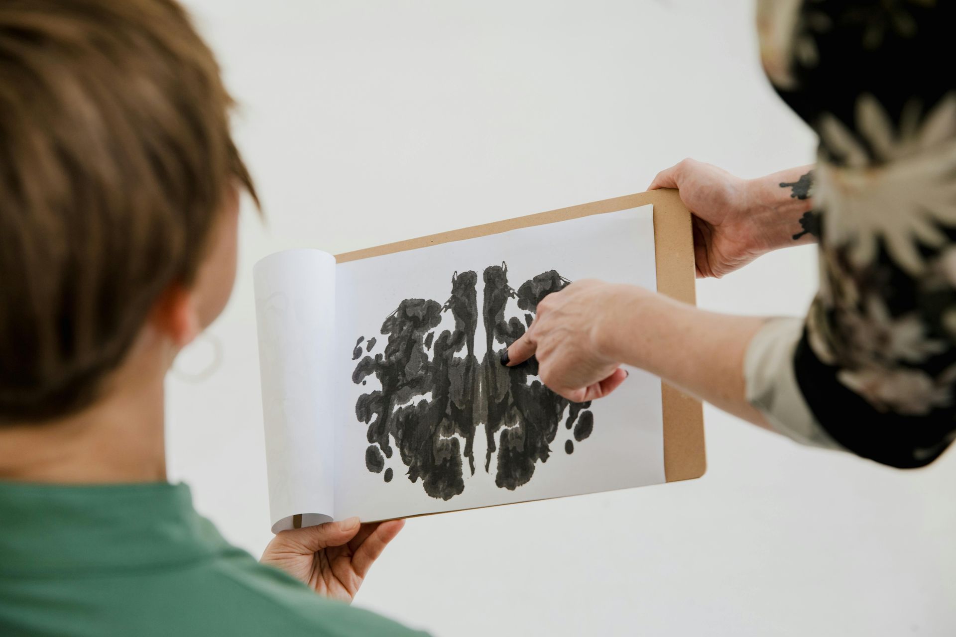 Unas manos sostienen un cuaderno de bocetos mientras otra persona señala un dibujo abstracto en negro.