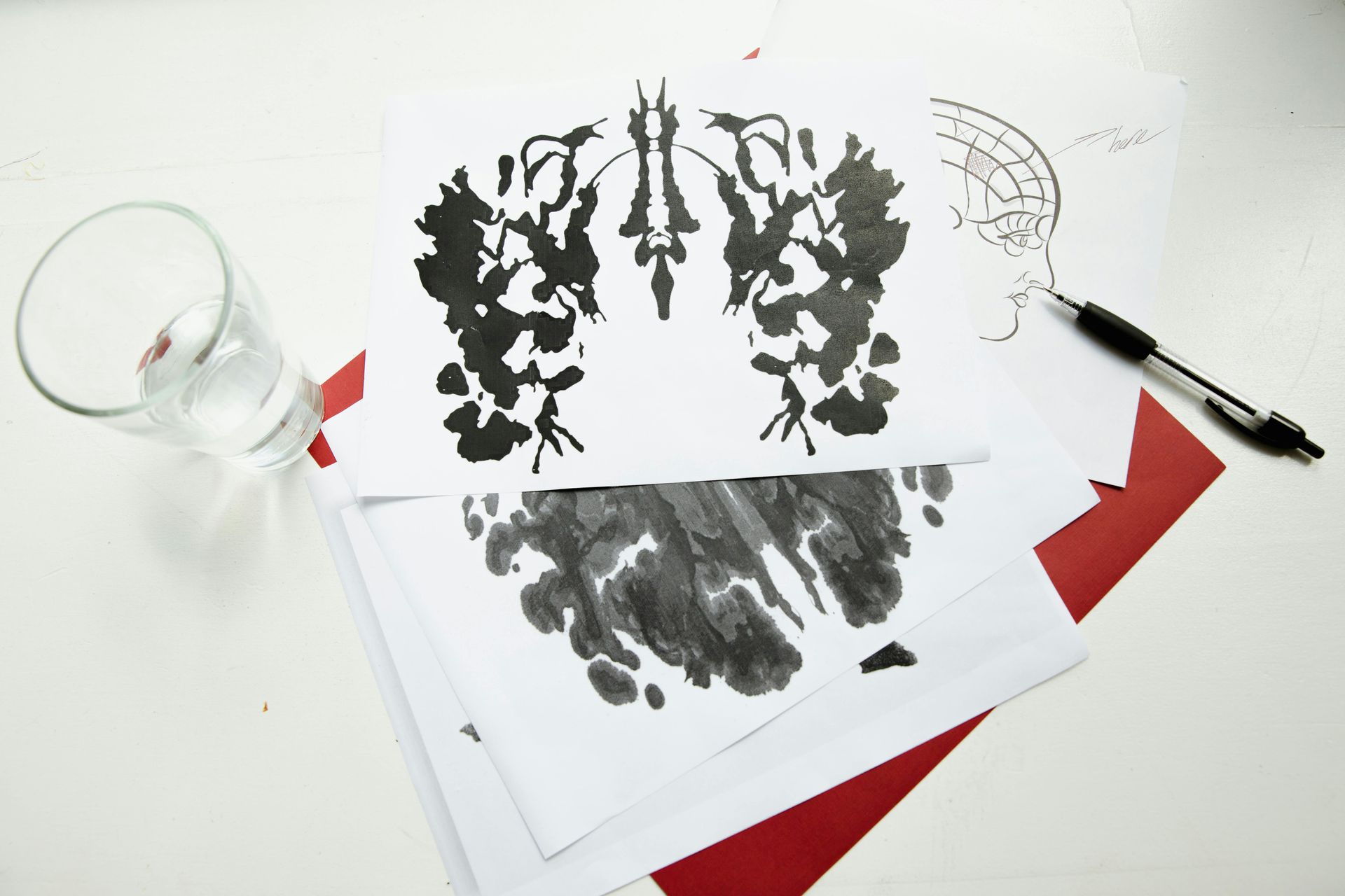 Herramientas de grabado y láminas entintadas sobre una mesa blanca con detalles de papel rojo.