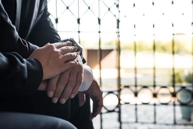 Un hombre y una mujer están sentados uno al lado del otro tomados de la mano.