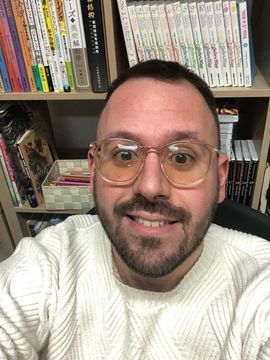 Persona somrient amb ulleres i un jersei blanc davant de prestatgeries de llibres o manga.