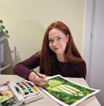 Dona pintant un paisatge verd a una taula amb materials d'aquarel·la