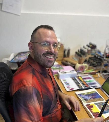 Persona somrient amb ulleres i un jersei blanc davant de prestatgeries de llibres o manga.