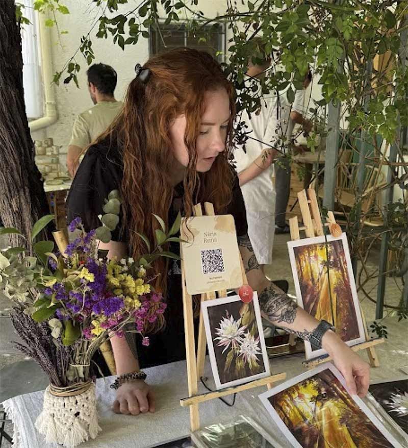 Dona pintant un paisatge verd a una taula amb materials d'aquarel·la