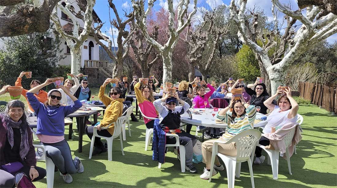 Gent asseguda en cadires blanques a l'aire lliure, aixecant les mans en un jardí assolellat reunida