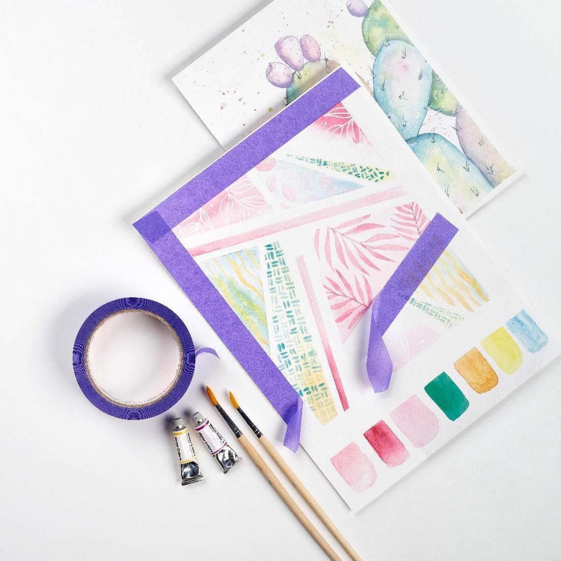 Dona en un estudi d'art, davantal, sostenint pinzells, examinant obres d'art a una taula.