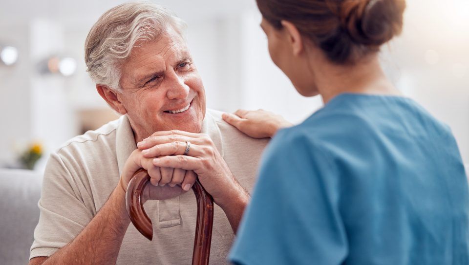 Ein älterer Mann mit einem Gehstock spricht mit einer Krankenschwester.