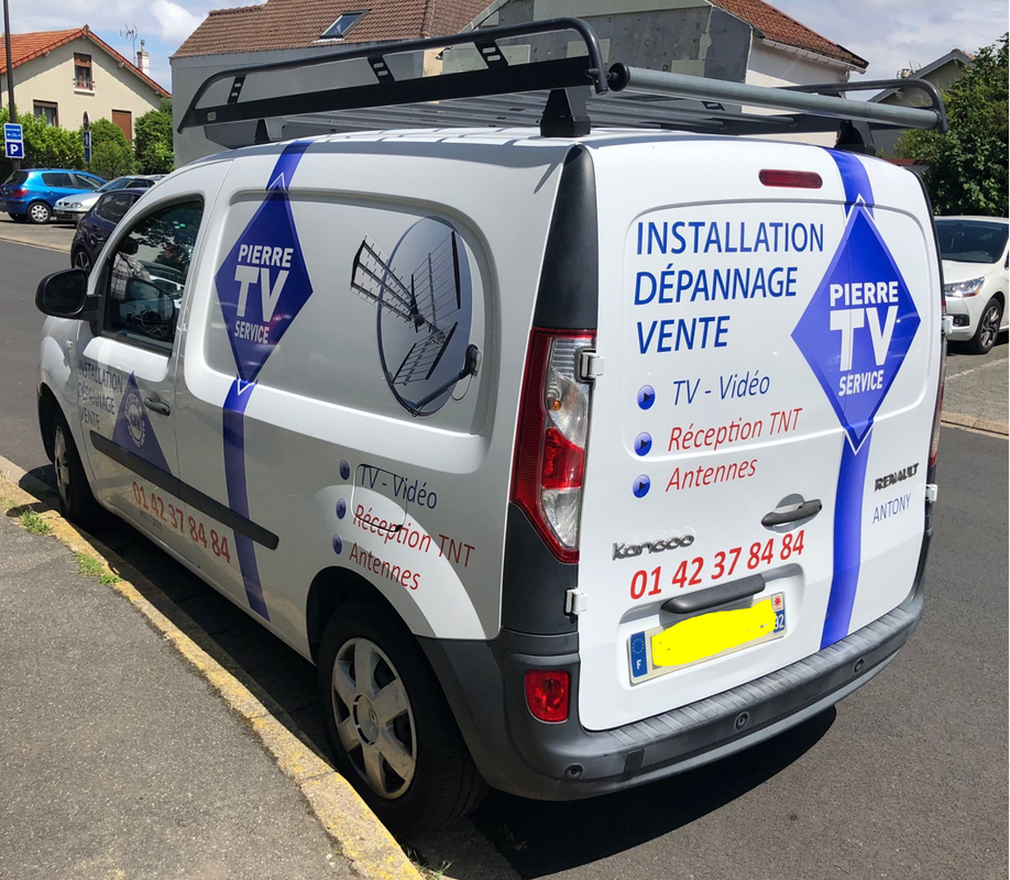 Une camionnette utilitaire Renault Kangoo blanche, garée dans la rue, arborant les logos, le numéro de téléphone et les services de Pierre TV Service.