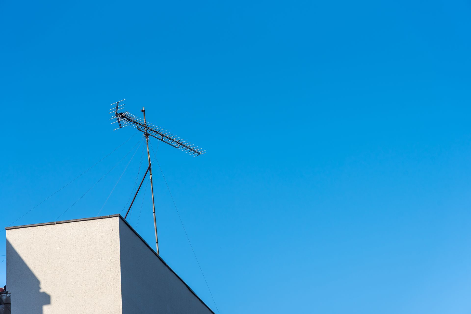 Une antenne de télévision en métal, fixée à l'angle d'un bâtiment, se détache sur un ciel bleu clair et lumineux.