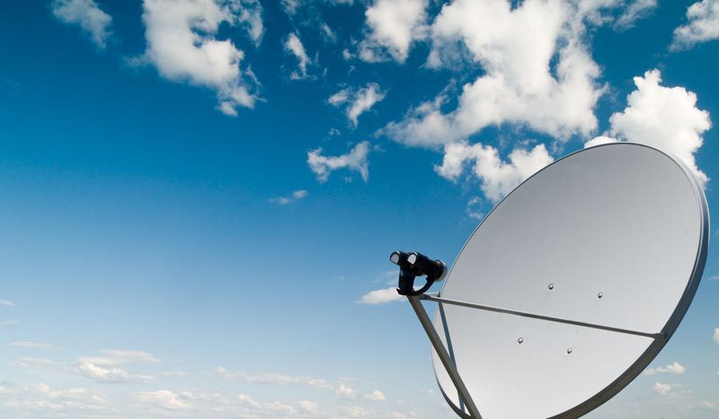 Une antenne de télévision et une parabole satellite se détachent sur un ciel bleu clair et lumineux.