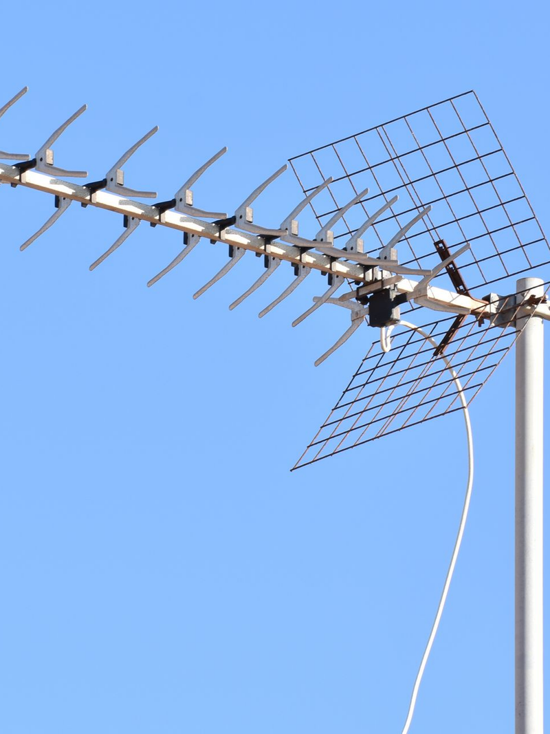 Une antenne de télévision et une parabole satellite se détachent sur un ciel bleu clair et lumineux.