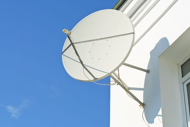 Une antenne parabolique blanche fixée sur le côté d'un bâtiment blanc, se détachant sur un ciel d'un bleu éclatant.