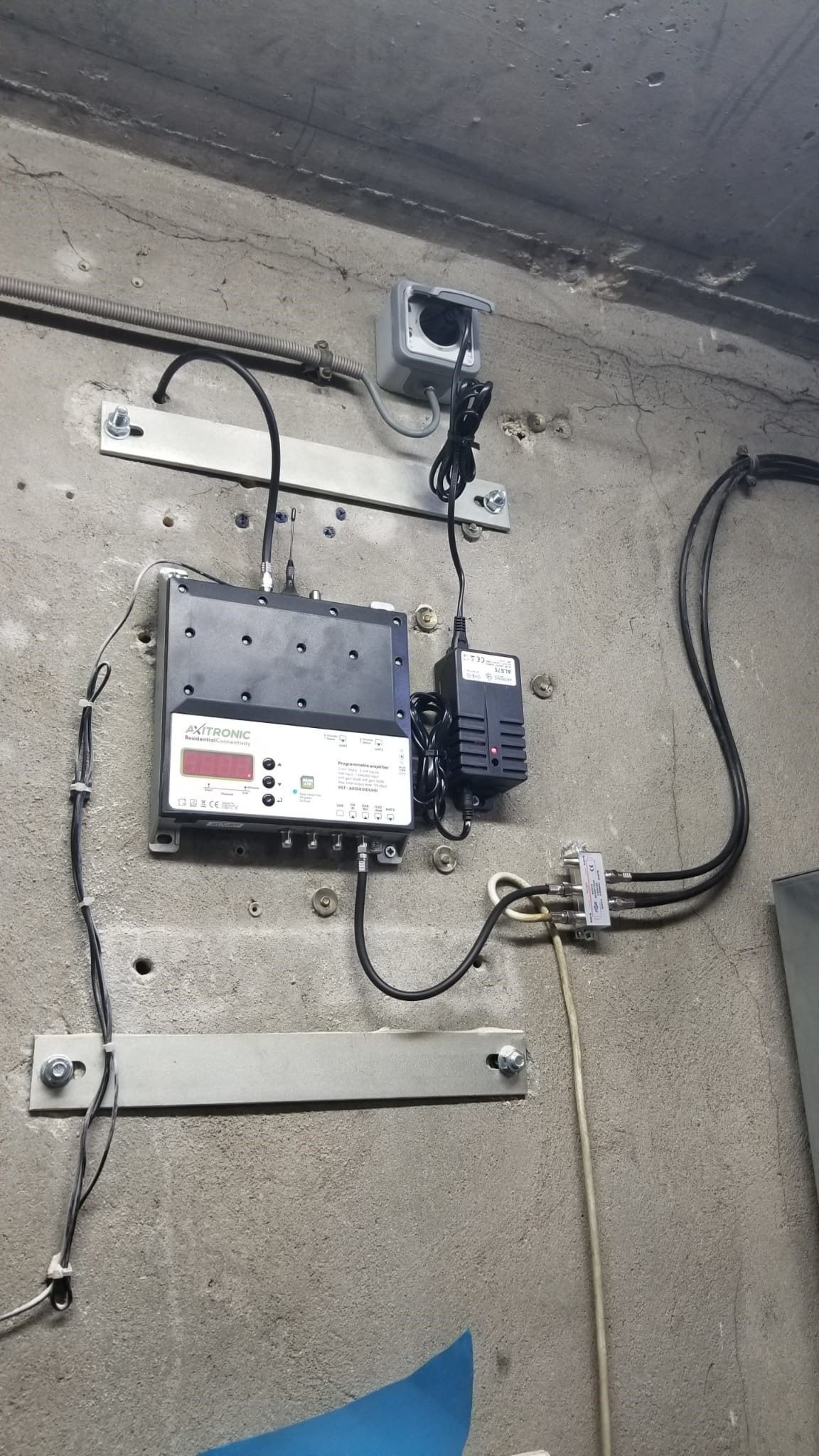 Un équipement électronique et une alimentation électrique fixés sur un mur en béton, reliés par des câbles noirs.