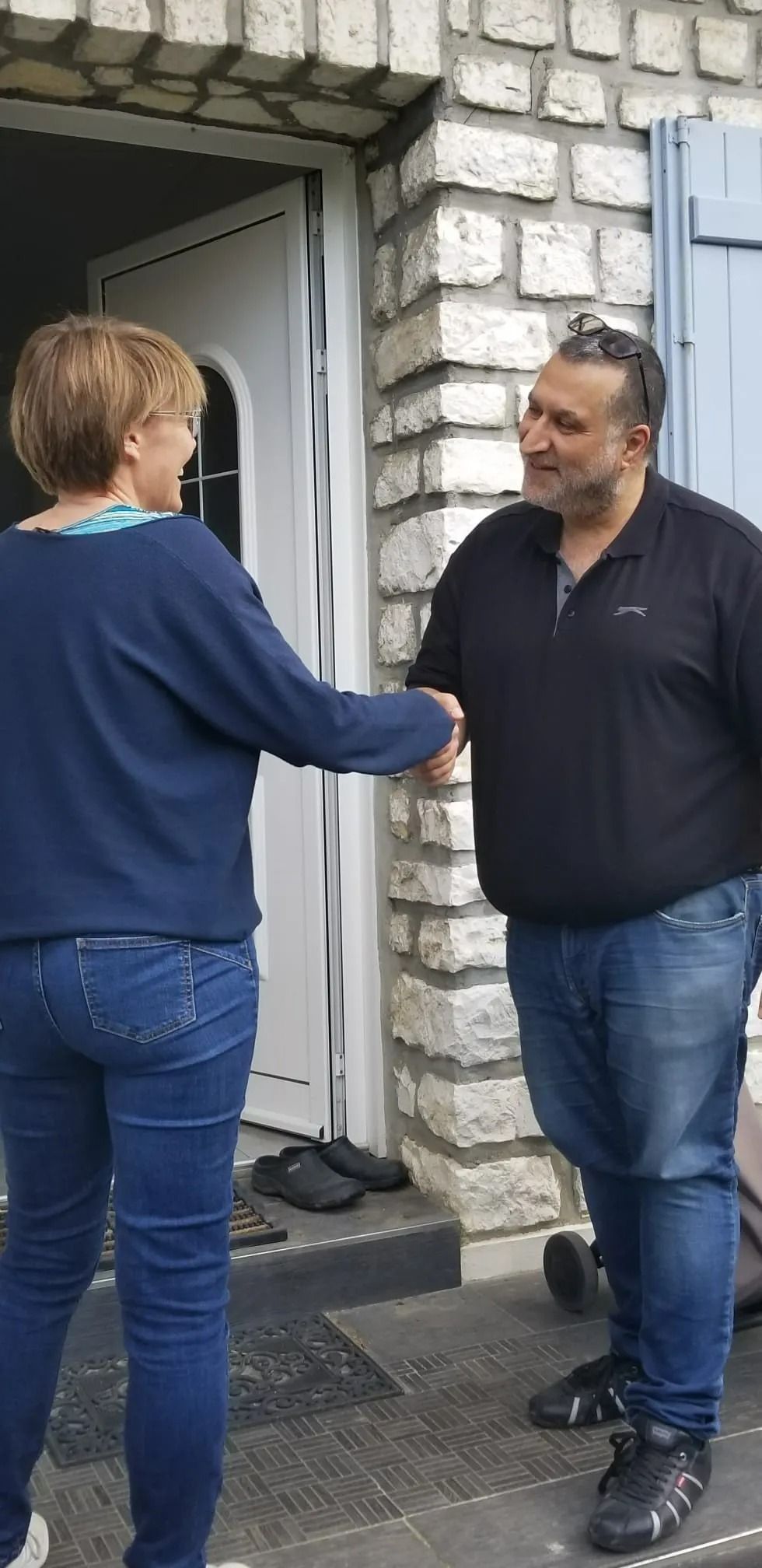 Deux personnes se serrent la main sur le seuil d'un bâtiment en pierre.