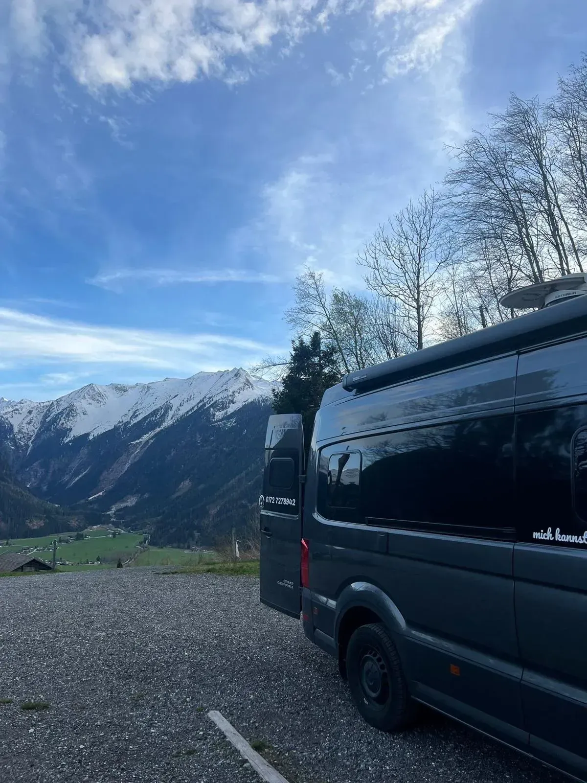 Ein schwarzer Lieferwagen ist auf einem Schotterplatz mit Bergen im Hintergrund geparkt.