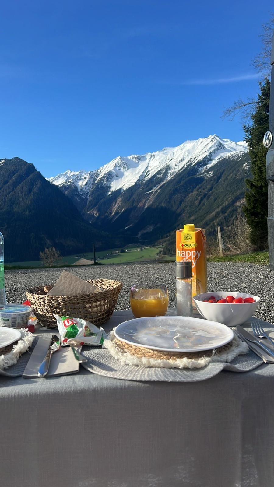 Ein Tisch mit Tellern, Schüsseln und einer Flasche Orangensaft darauf mit Bergen im Hintergrund.