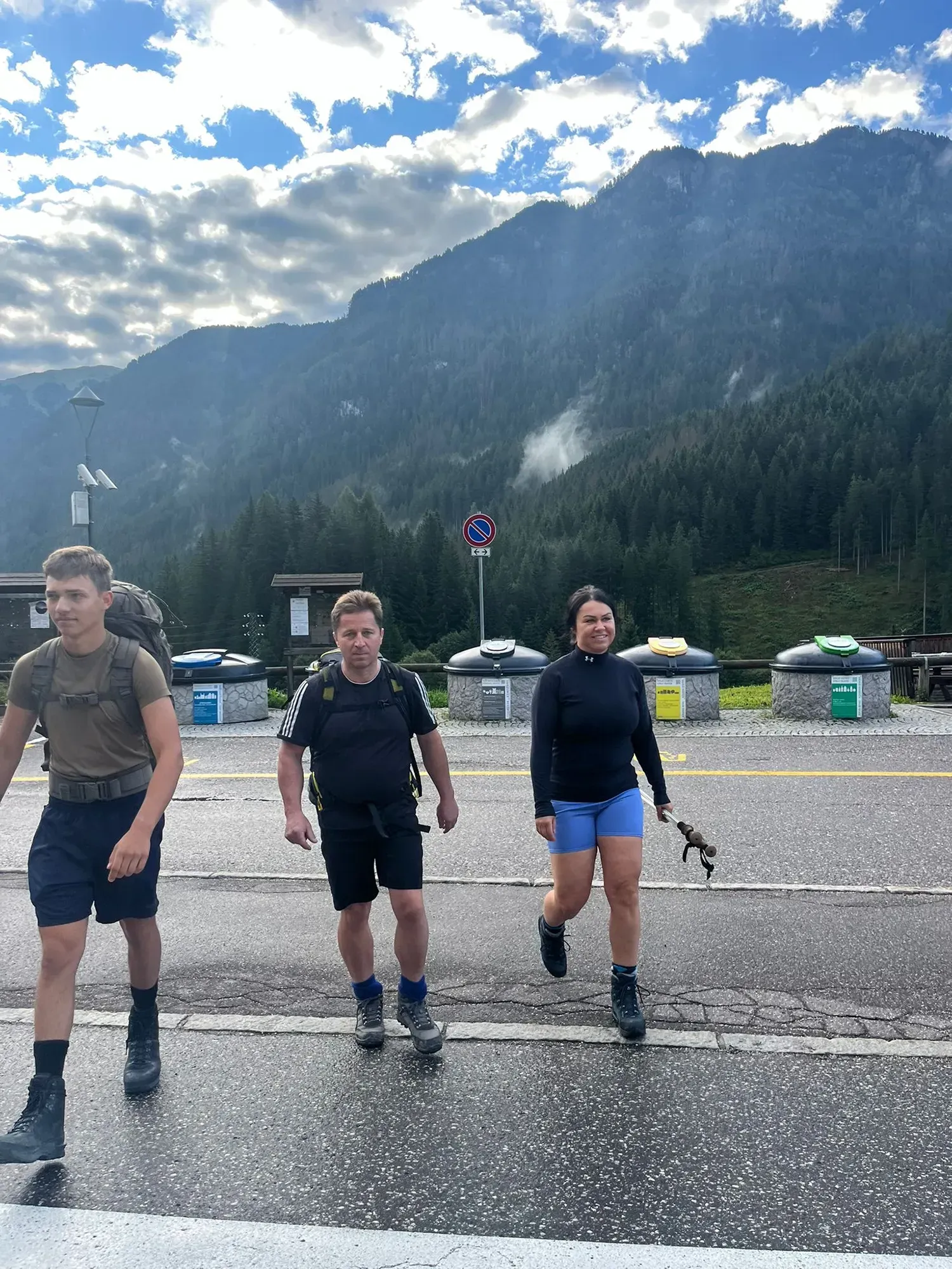 Drei Personen gehen eine Straße entlang, im Hintergrund sind Berge