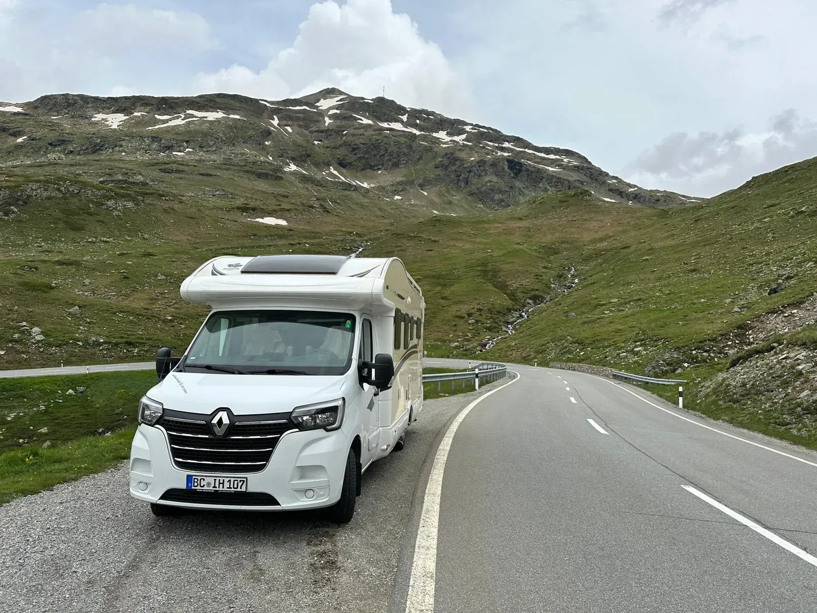 Ein weißes Wohnmobil ist am Rand einer Bergstraße geparkt.