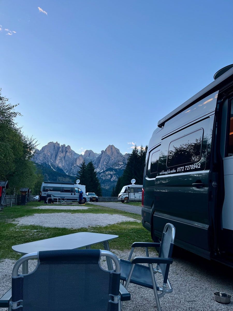 Ein Lieferwagen ist neben einem Tisch und Stühlen auf einem Campingplatz mit Bergen im Hintergrund geparkt.