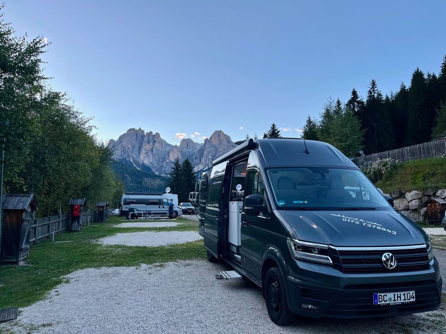 Ein Volkswagen Transporter steht auf einem geschotterten Parkplatz mit Bergen im Hintergrund.