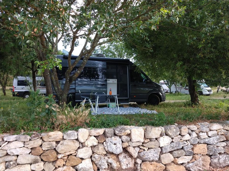 Ein schwarzer Lieferwagen parkt auf einem Feld neben einer Steinmauer.