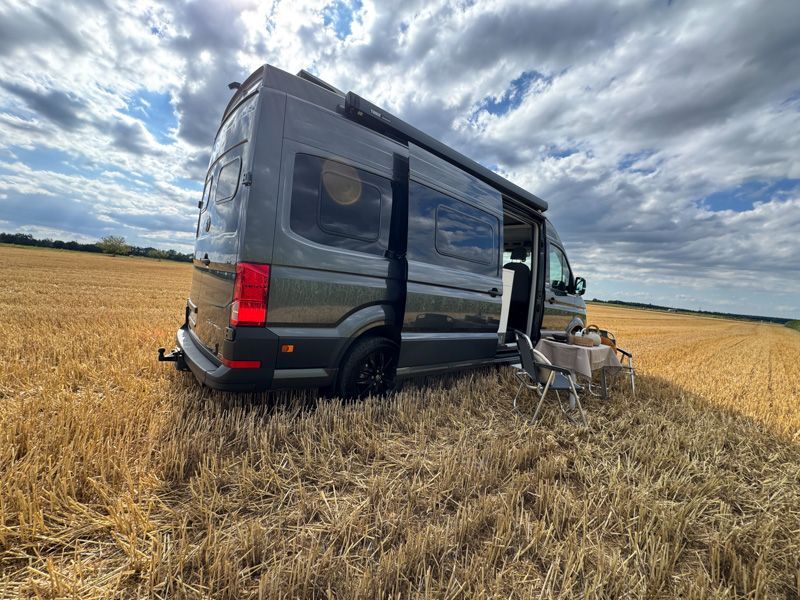 Ein dunkelgrauer Lieferwagen parkt in einem Weizenfeld unter bewölktem Himmel.