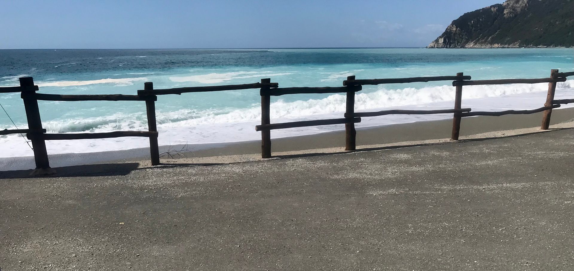 Ein Holzzaun umgibt einen Strand mit dem Meer im Hintergrund