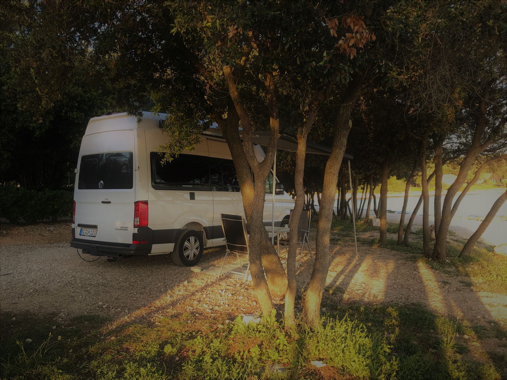 Ein weißer Lieferwagen steht unter einem Baum auf einem Parkplatz.