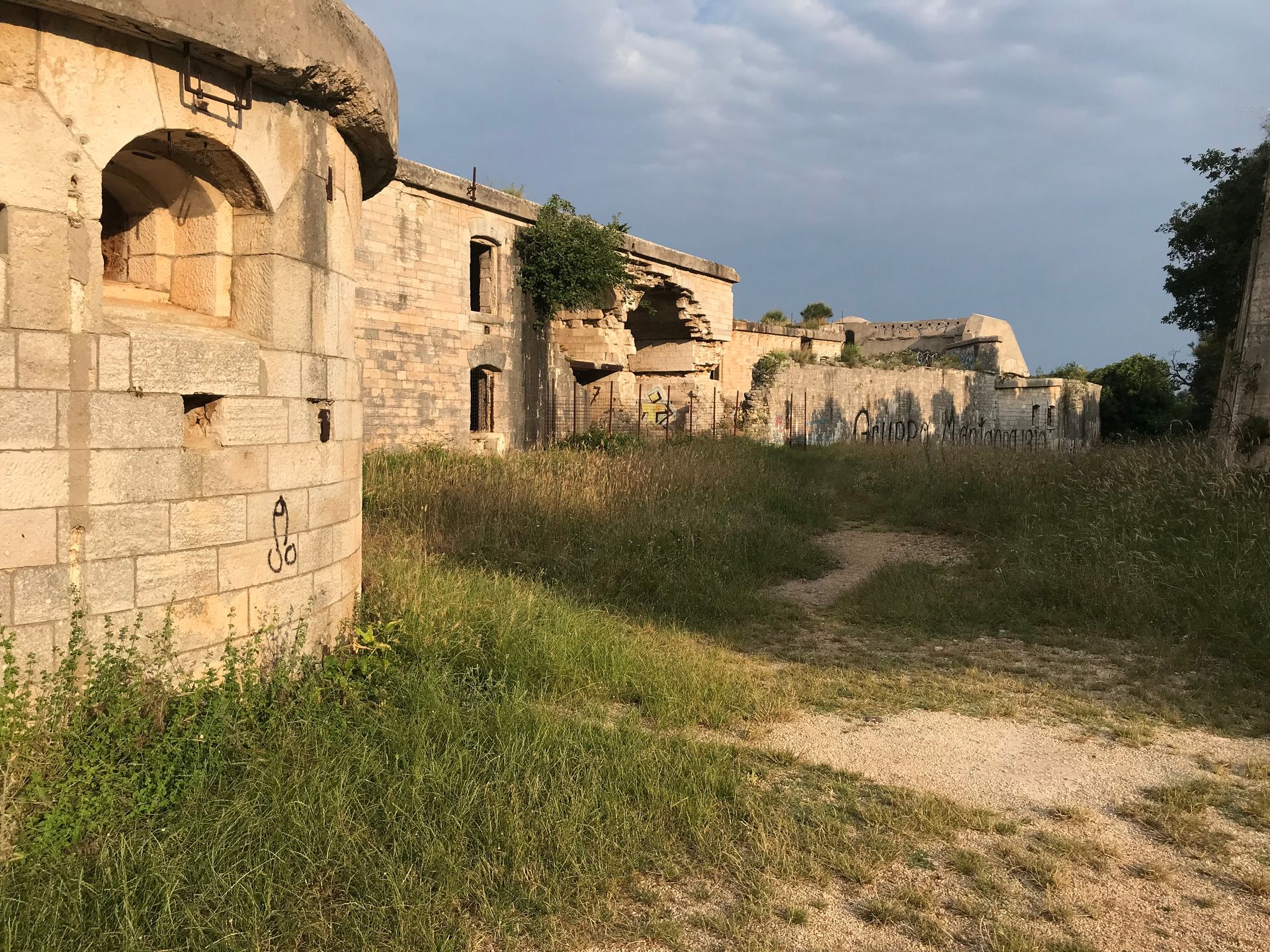 Ein Backsteingebäude ist von hohem Gras und einem Feldweg umgeben.