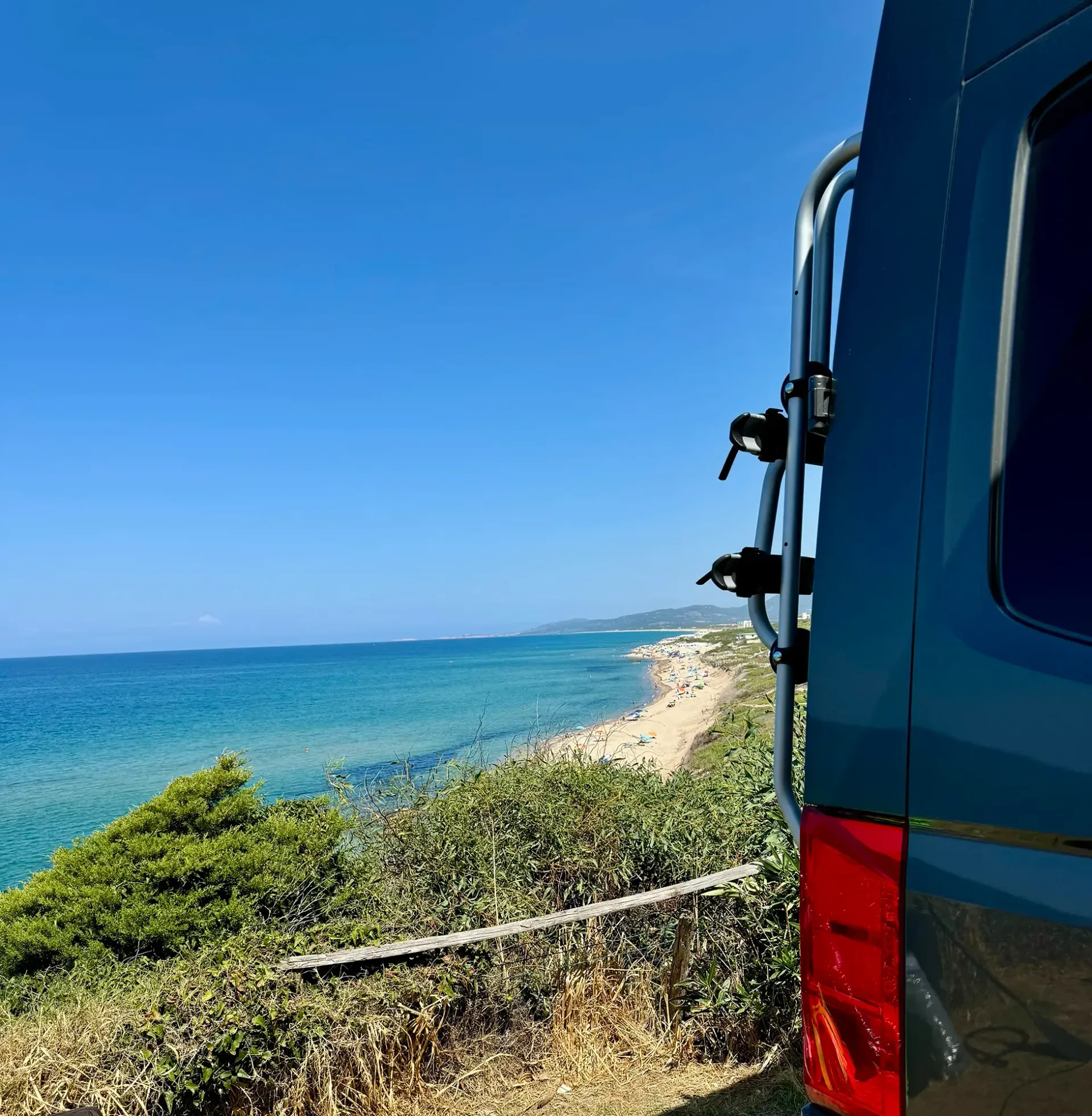 Ein blauer Van steht auf einem Hügel mit Blick auf den Ozean