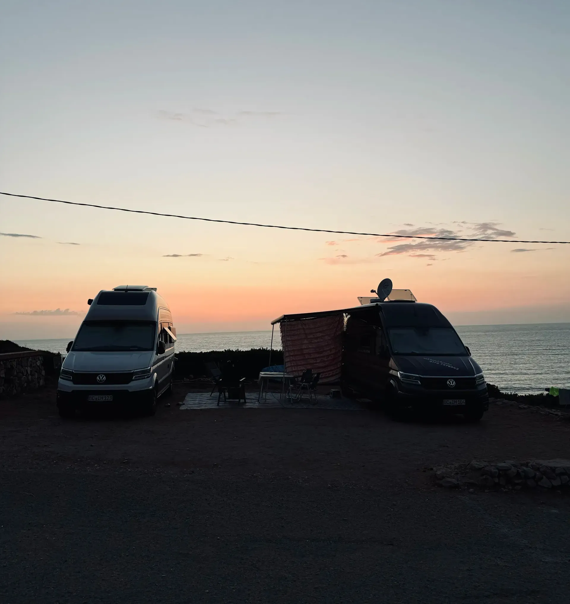 Zwei Lieferwagen stehen bei Sonnenuntergang vor dem Meer