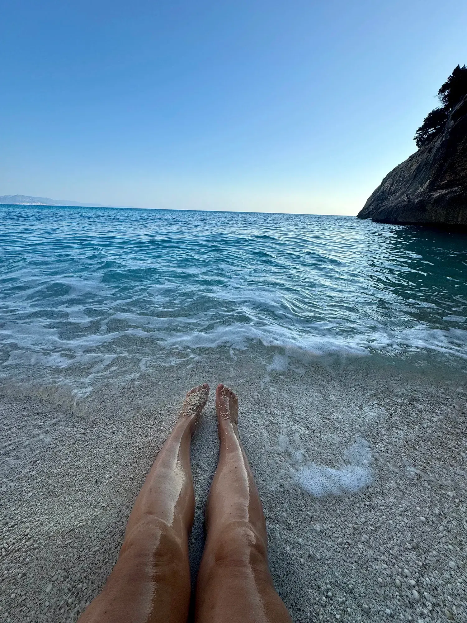 Eine Person liegt mit den Füßen im Wasser am Strand.