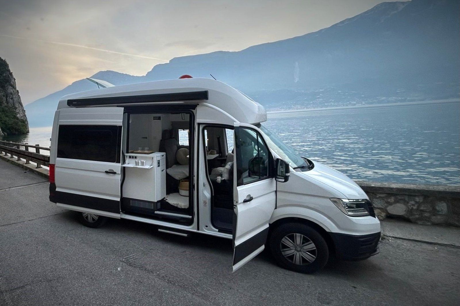 Ein weißer Lieferwagen steht am Straßenrand neben einem See.