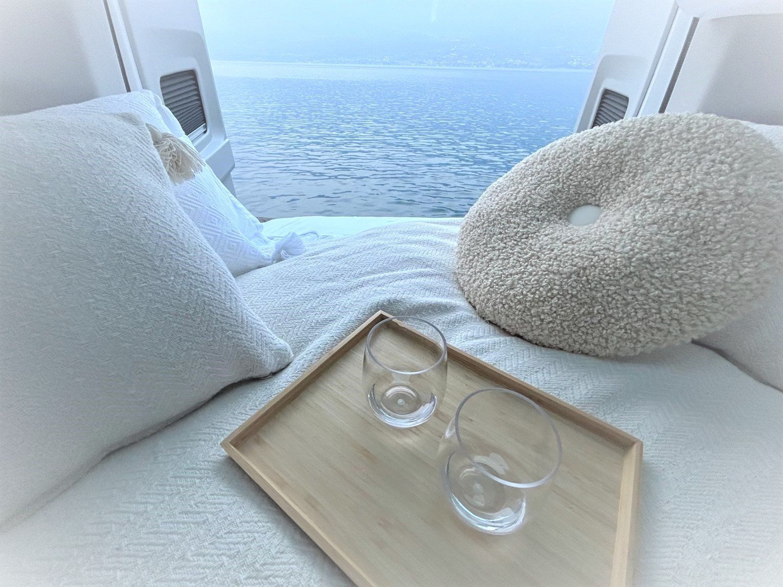 Ein Tablett mit zwei Gläsern steht auf einem Bett neben einem Fenster mit Blick auf das Meer.