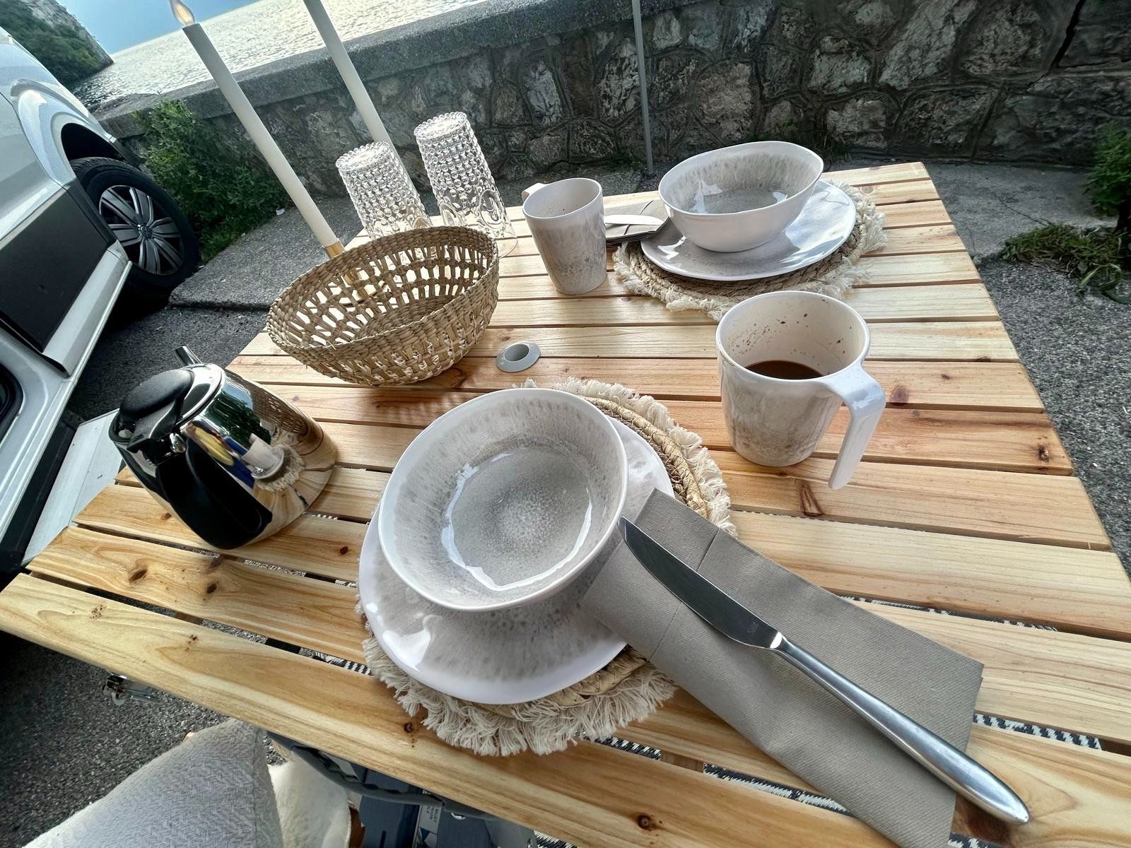 Ein Holztisch mit Tellern, Schüsseln, Tassen und Besteck darauf.