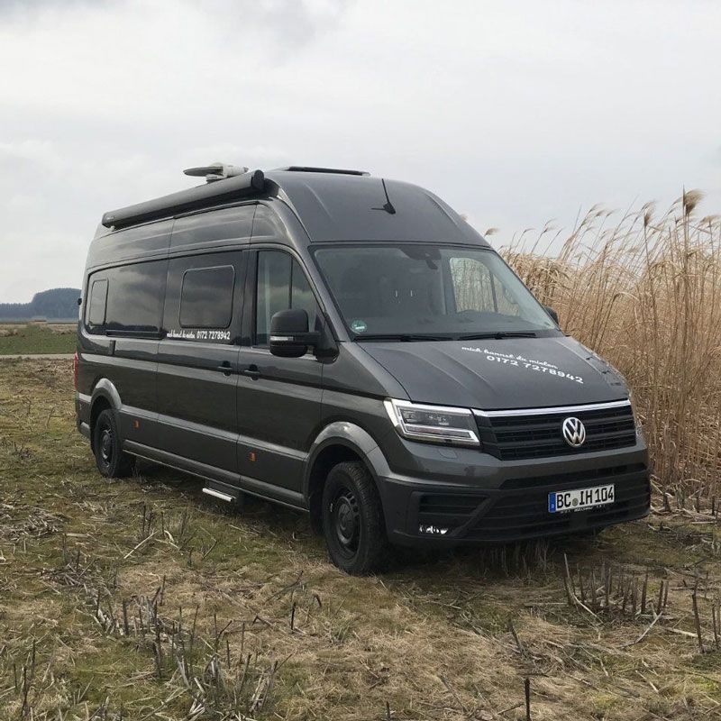 Ein Volkswagen Transporter ist auf einem Feld mit hohem Gras geparkt.