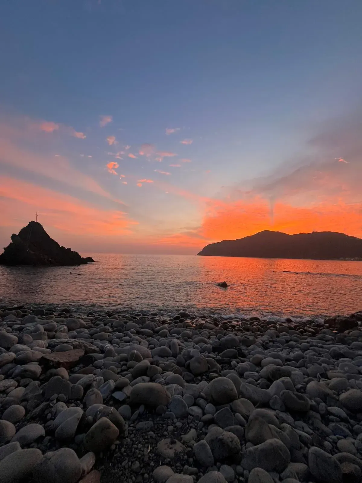 Ein Sonnenuntergang über dem Meer mit einem felsigen Strand im Vordergrund
